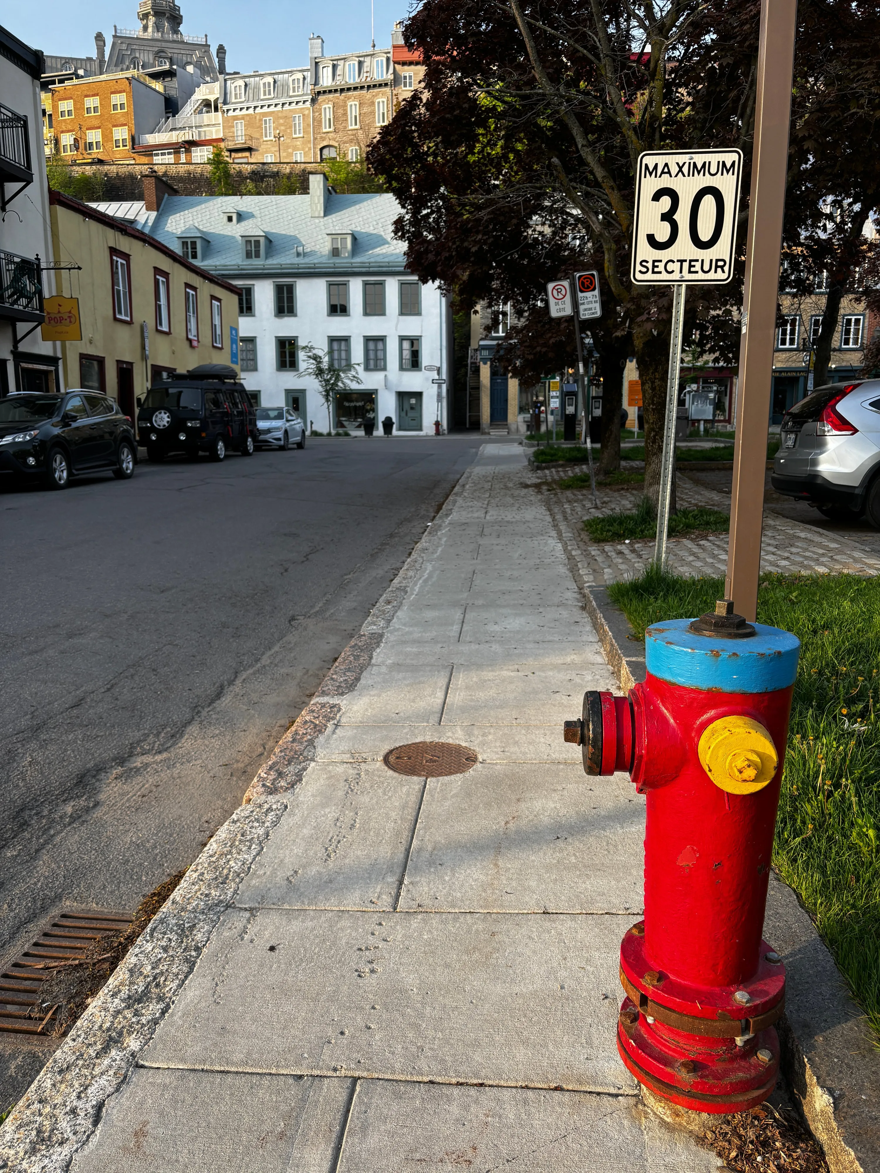A red fire hydrant with a blue top beside a footpath, a 30 speed limit sign and old buildings in morning light